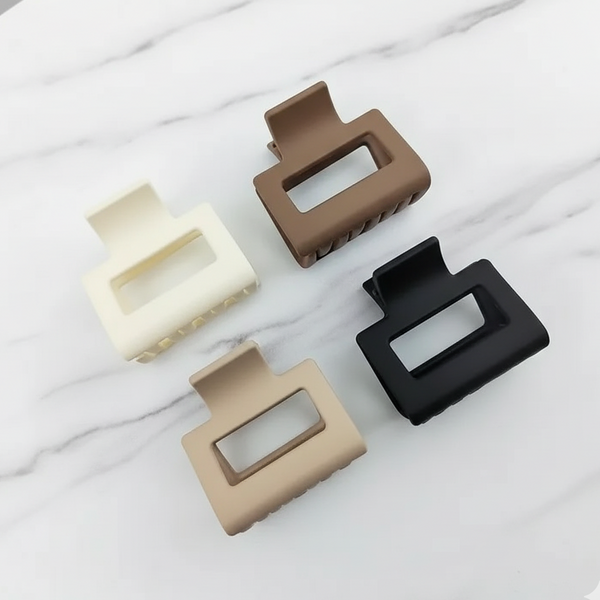 Four rectangular hair clips in beige, brown, black, and white on a marble surface.