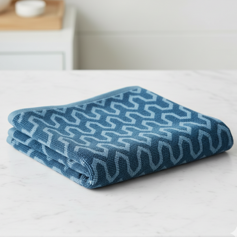 Folded blue towel with wavy pattern on a white surface