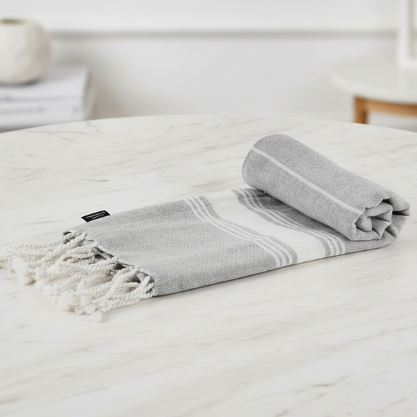 Grey towel with white stripes and fringes on a white surface